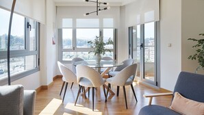 Een moderne woonkamer met een ronde glazen tafel, grijs gestoffeerde stoelen, een grijze bank en een groot raam met uitzicht op de stad.