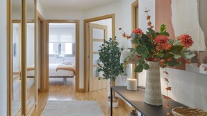 Een gang met een bed, een potplant, een vaas met bloemen en een spiegel.