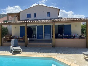 A two-story house with a covered patio, a swimming pool, and a dining area with outdoor furniture.