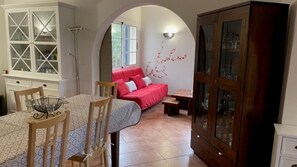 Uma área de jantar com uma mesa posta para dois, um sofá vermelho e um armário com portas de vidro.