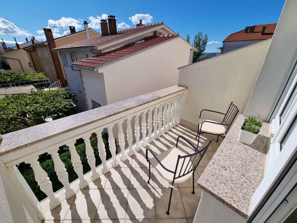 A balcony with a white balustrade, a single chair, and a small potted plant.