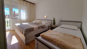 A bedroom with two beds, a sliding glass door, a bedside lamp, and a potted plant. - Holiday apartment with balcony and air conditioning (Crikvenica)