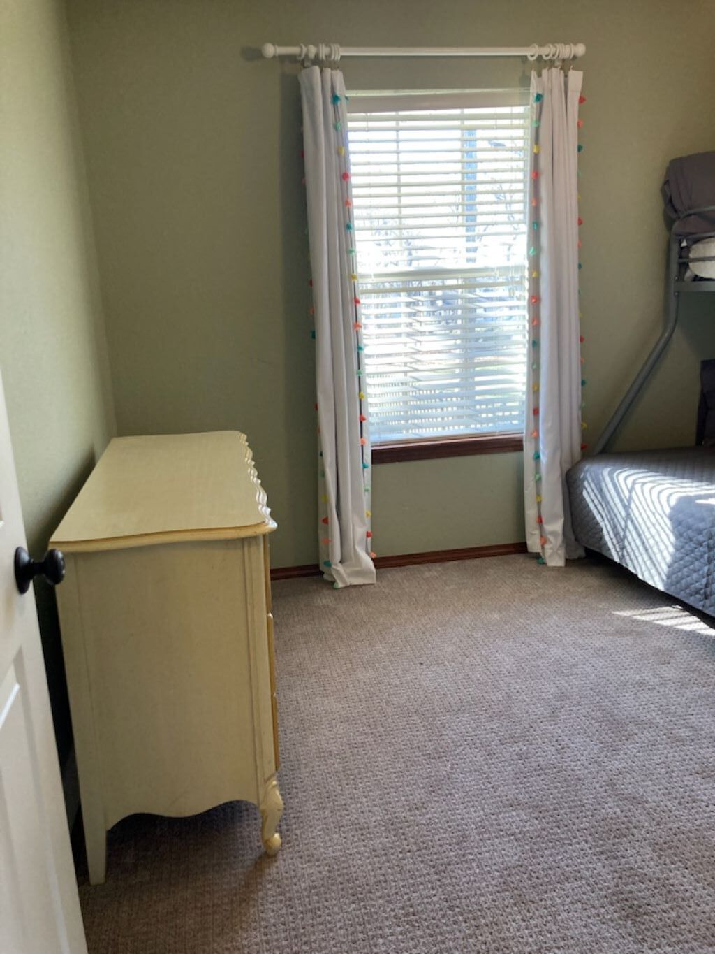 A room with a bunk bed, a small table, and a window with curtains.