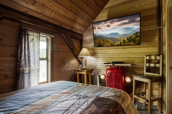 Une chambre rustique en bois, avec un lit, une fenêtre avec des rideaux, un téléviseur fixé au mur et un radiateur rouge.