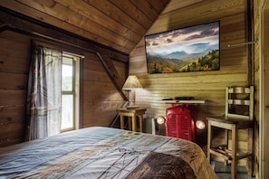 Une chambre rustique en bois, avec un lit, une fenêtre avec des rideaux, un téléviseur fixé au mur et un radiateur rouge.