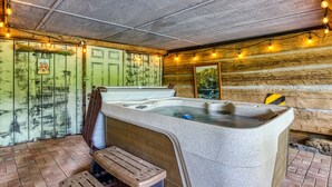 Een rustieke wellnessruimte met een stenen hottub, houten banken en lichtslingers.