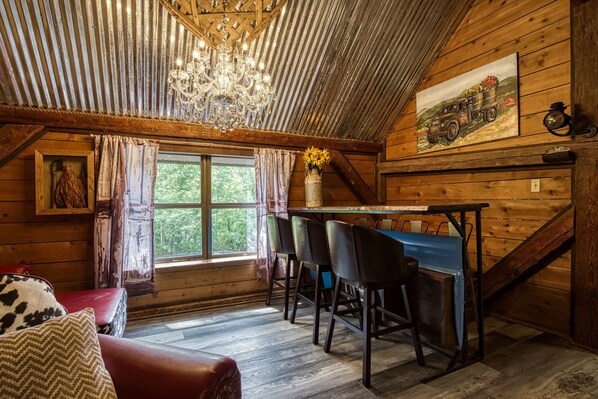 A rustic wooden interior with a dining area, a chandelier, and a painting of a vintage truck. - Gatlinburg | Arcade | Pet Friendly | Hot Tub | Secluded | WiFi (Gatlinburg)