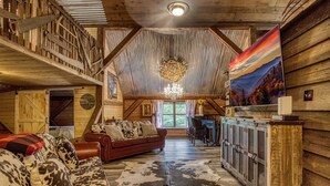 Een rustiek houten interieur met een slaaploft, een eethoek en een woonkamer, ingericht met een rode bank en een kleden van koeienhuid.