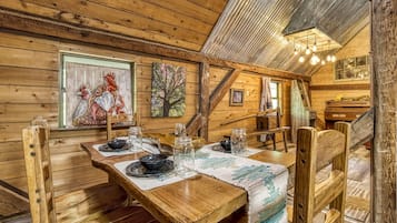 A rustic wooden dining area with a table set for two, wooden chairs, and a ceiling with exposed beams.