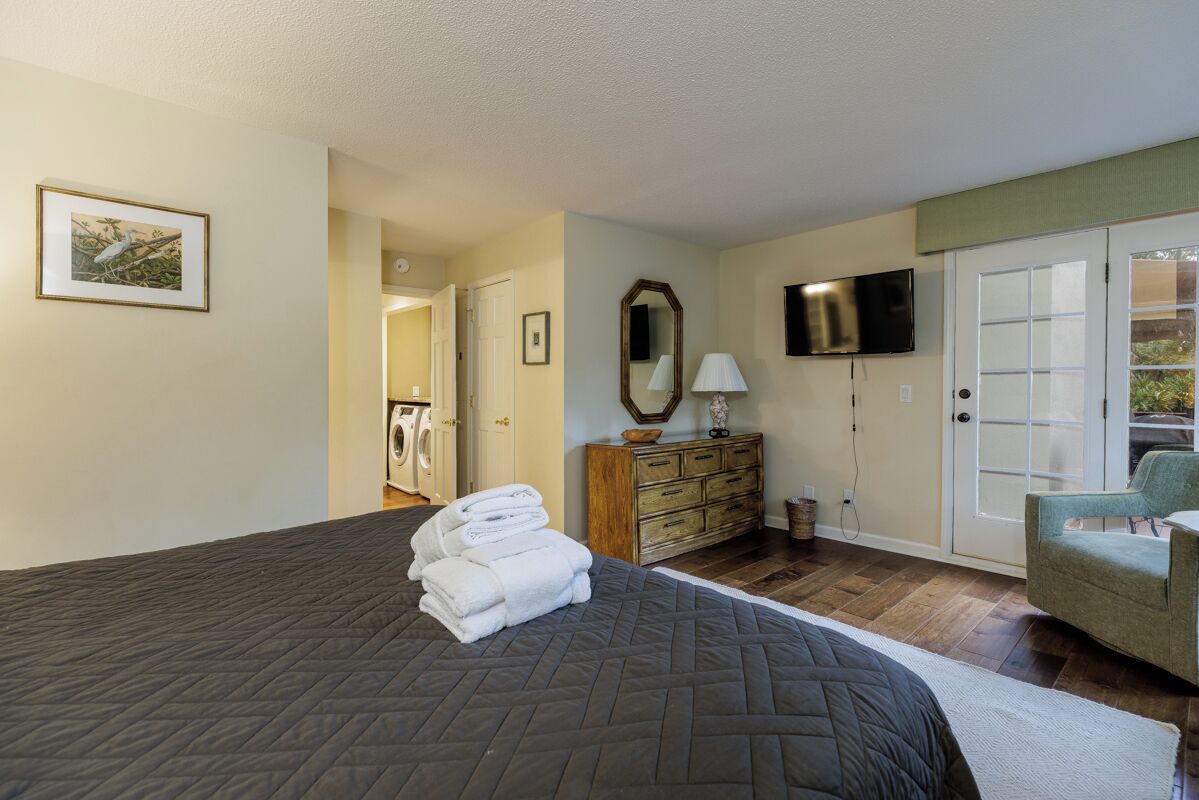 A bedroom with a large bed, a dresser, a TV, and a door leading to a balcony.