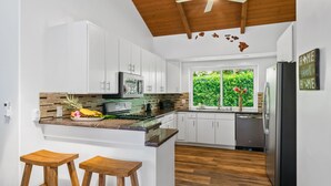 A modern kitchen with white cabinets, a wooden ceiling, and a view of greenery outside. - Laule'a 'Ohana Hale - Luxurious 'Ohana home with A/C (Princeville)