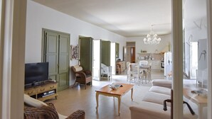 Een ruime woonkamer met een televisie, een eethoek met tafel en stoelen, en een keuken op de achtergrond.