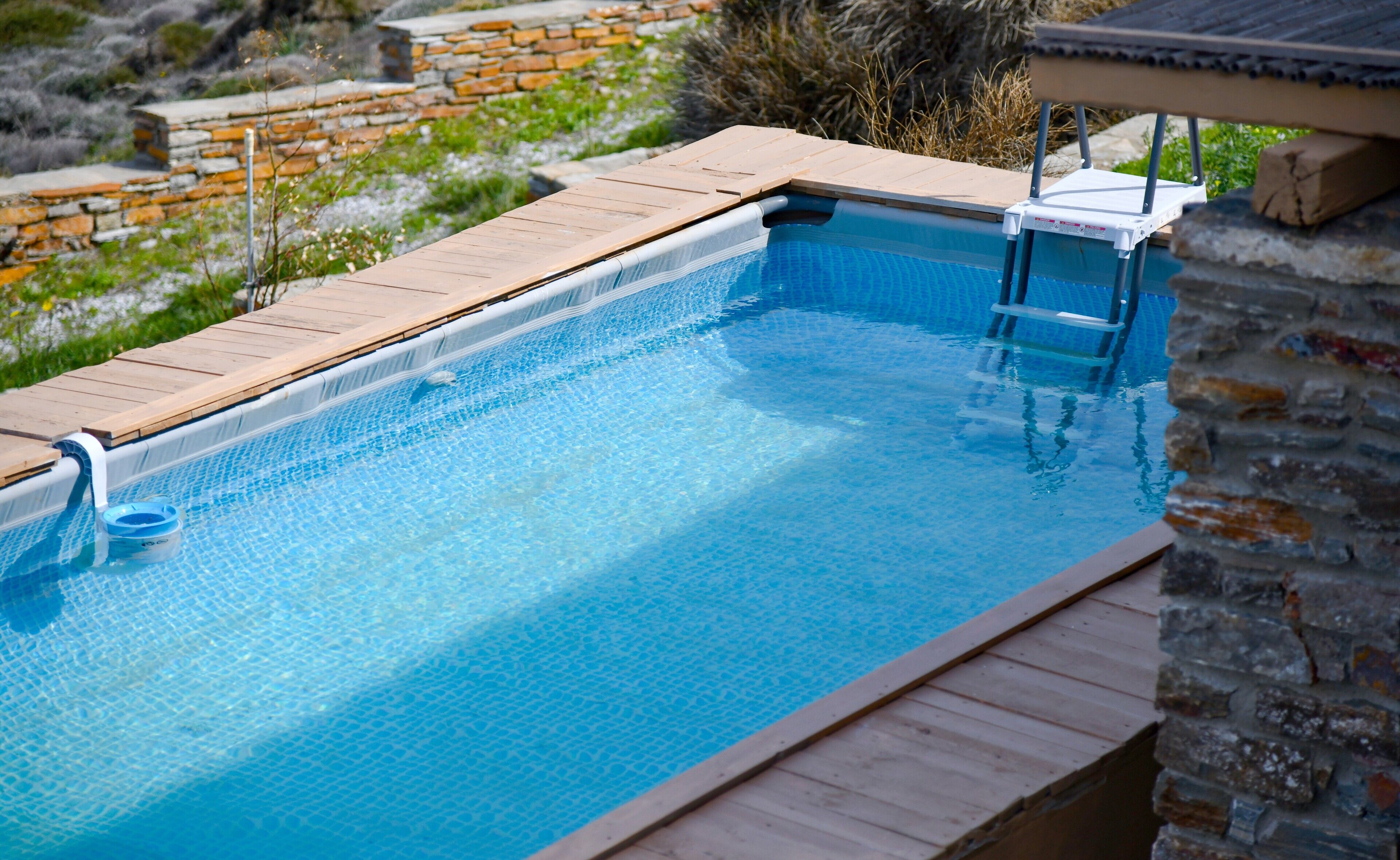 A swimming pool with a wooden deck and a stone wall in the background.