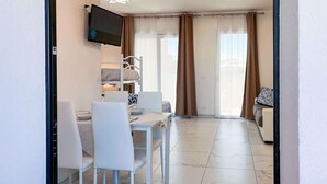 Une pièce comprenant une table à manger, des chaises, un téléviseur fixé au mur, un lit superposé et une porte-fenêtre coulissante donnant sur un balcon.