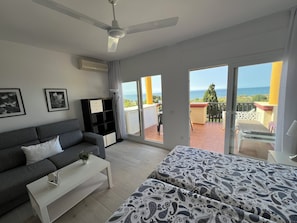 A modern living room with a sofa, a coffee table, a bed with patterned bedding, a ceiling fan, and a view of the sea through large sliding doors. - Apartment 817 on the waterfront with a view of the sea (Marbella)