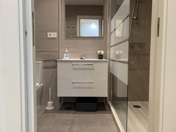 A modern bathroom with a glass shower enclosure, a white sink with a mirror above, and a small vase with flowers on the countertop. - Apartment 817 on the waterfront with a view of the sea (Marbella)