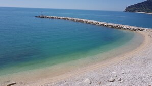 Ein Strand mit klarem, blauem Wasser, einem steinernen Wellenbrecher und einem Kiesufer.