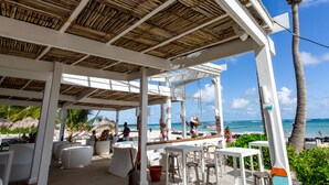 Un espacio al aire libre techado con muebles blancos, techo de madera y vistas a la playa y al océano.