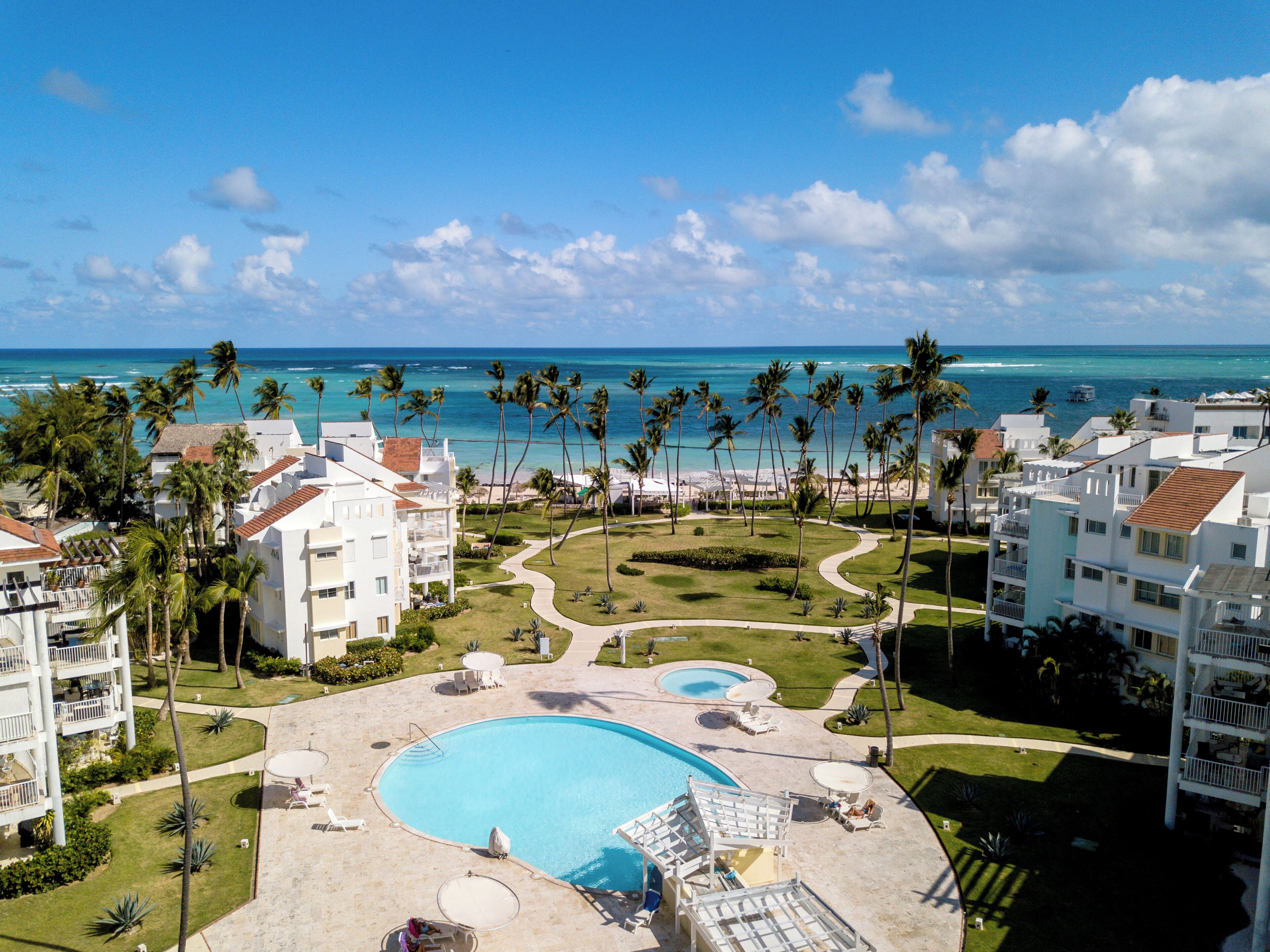 A resort with a large swimming pool, palm trees, and a view of the ocean.