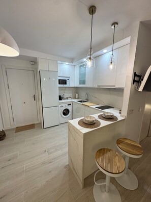A modern kitchen with white cabinetry, a built-in washing machine, and a central island with stools. - Apartment 853 on the waterfront with a view of the ocean (Marbella)