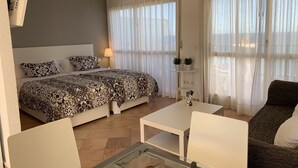 Et moderne hotelværelse med en seng, en sofa, et glasbord og et lille sidebord med lampe og fjernbetjeninger.