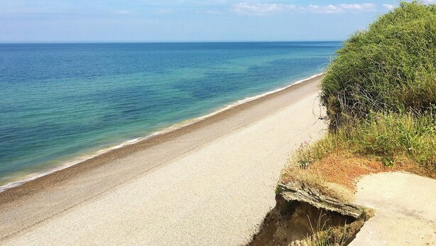 A coastal road with a clear view of the sea and a grassy area on the right. - Coastguard's Cottage (Weybourne)