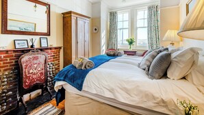 A well-lit bedroom with a large bed, a dresser, a mirror, and a window with curtains. - Coastguard's Cottage (Weybourne)