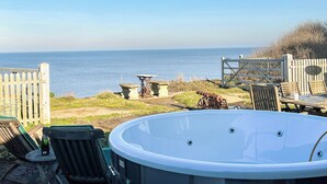 A patio with a hot tub, wooden chairs, and a view of the sea. - Coastguard's Cottage (Weybourne)