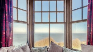 A view through a large window with a view of the sea and grassy landscape. - Coastguard's Cottage (Weybourne)