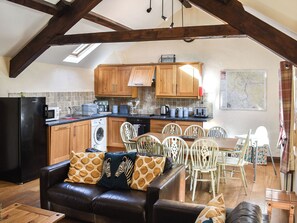 A kitchen with wooden cabinets, a black refrigerator, and a dining area with a brown leather couch and white chairs. - Mount Cottage-UK42230 (Near Tebay)
