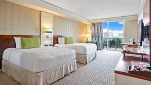 A hotel room with two beds, a desk, a chair, a TV, and a balcony with a city view. - Beachfront Suite: Resort Amenities Included (Sunny Isles Beach)