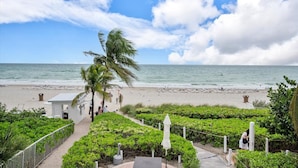 A beach with a white building, a palm tree, and a view of the ocean. - Beachfront Suite: Resort Amenities Included (Sunny Isles Beach)