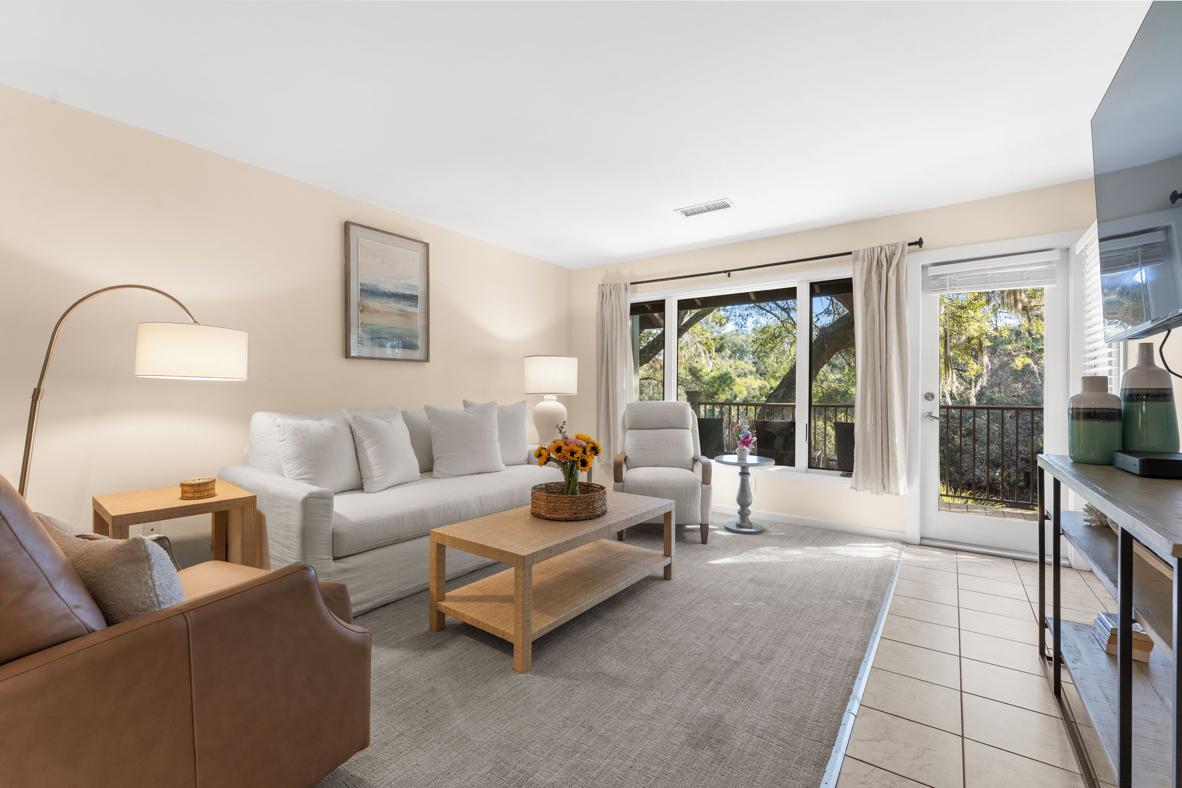 A modern living room with a sofa, armchair, and coffee table, a dining area with a table and chairs, and large windows with curtains.