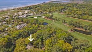 Luftaufnahme eines Golfplatzes mit einem großen Wasserlauf links, umgeben von dichtem Grün und Wohngebäuden.