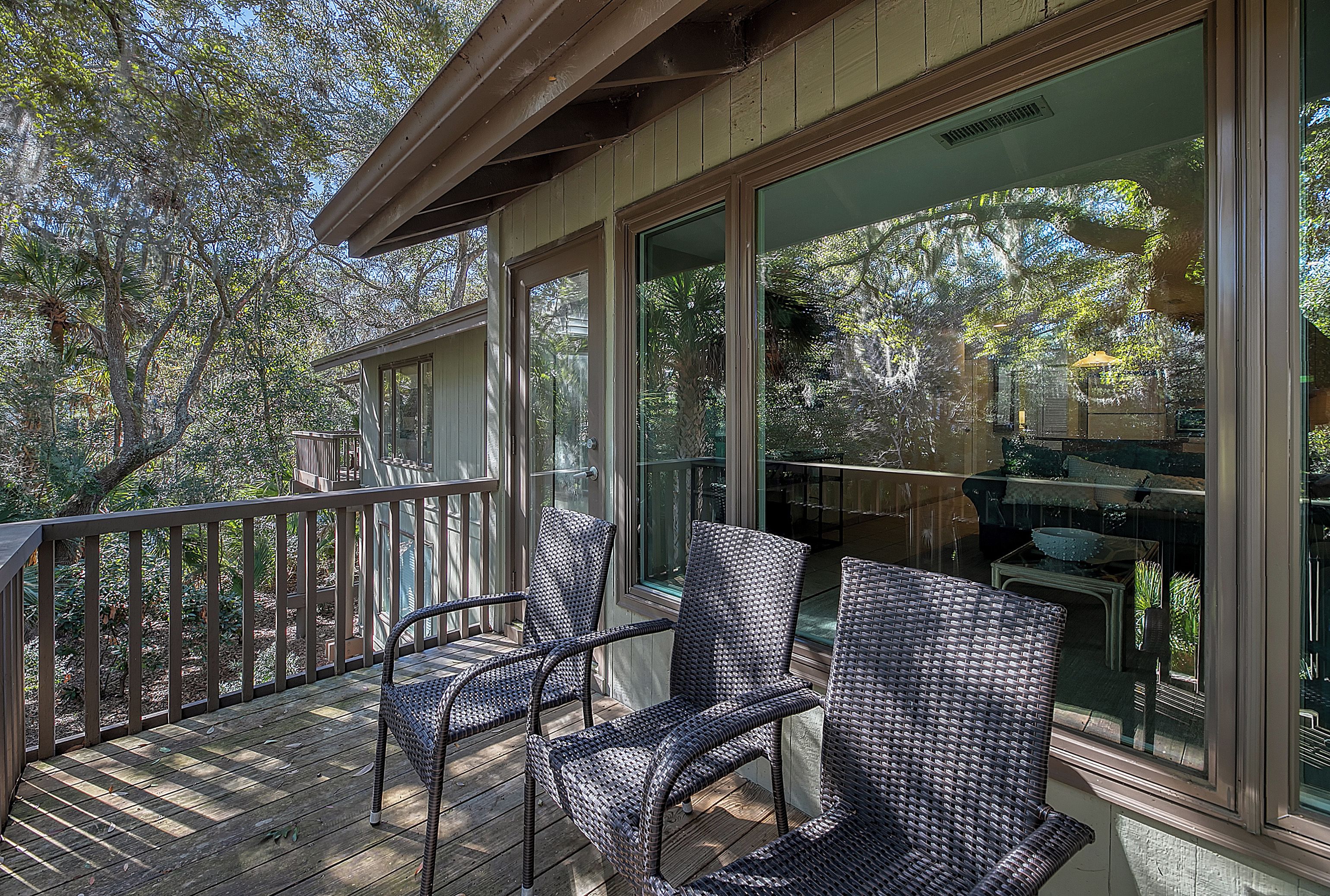 A wooden deck with wicker chairs and large windows overlooking a garden.