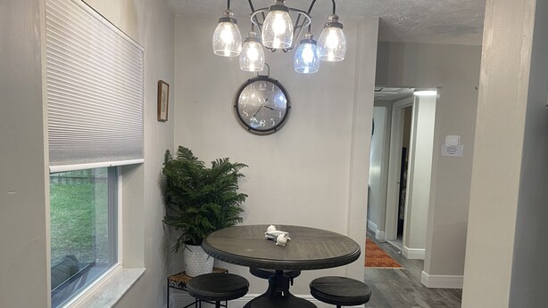 A dining area with a round table, four stools, a potted plant, a wall clock, and a ceiling light fixture. - Available August 22-28! Cute and cozy (Ocala)