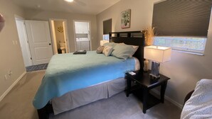 A bedroom with a bed, nightstands, a ceiling fan, a window with blinds, and a door leading to a bathroom. - Available August 22-28! Cute and cozy (Ocala)