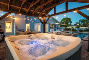 Un bain à remous surmonté d’une pergola en bois, entouré de chaises longues et d’une piscine.