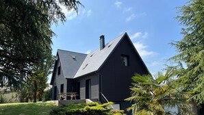Una casa moderna con fachada oscura, techo inclinado y chimenea visible.