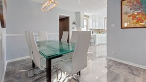 Een moderne eethoek met een glazen tafel en witte stoelen, een keuken op de achtergrond en een kaart aan de muur.