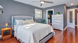 Un dormitorio con cama, mesitas de noche, cómoda y ventilador de techo.