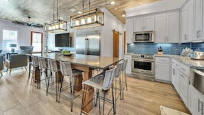 A modern kitchen with a central island, stainless steel appliances, and a dining area with bar stools. - Upscale Destin Escape Pool Golf Cart Beach Access (Miramar Beach)