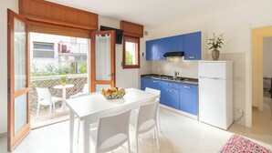 Een moderne keuken met blauwe kastjes, een witte koelkast en een eethoek met een tafel en stoelen.