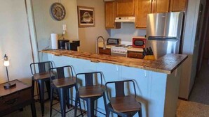 Una cocina compacta con una isla central, taburetes de bar, un refrigerador, un microondas y una estufa.