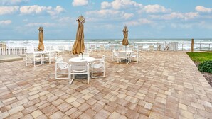 Un patio con sillas y mesas blancas, sombrillas color crema y vista al océano.