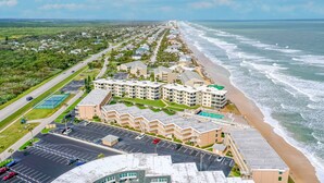 Vista aérea de un hotel costero con varias construcciones, un estacionamiento y acceso directo a la playa.