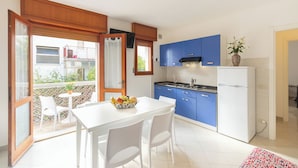 A modern kitchen with blue cabinets, a white refrigerator, and a dining area with a table and chairs.