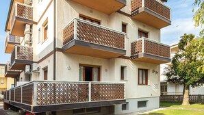 A multi-story building with balconies, a paved entrance, and a well-maintained lawn.