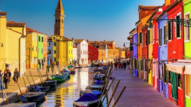 A canal with boats, colorful buildings, and a tower.