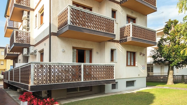 Un edificio residencial de varios pisos con balcones, entrada pavimentada y césped bien cuidado.